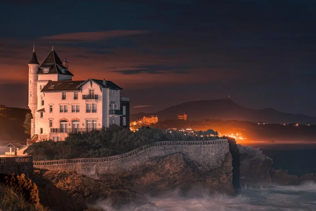 Un château se dresse au sommet d’une falaise la nuit, une scène qui pourrait expliquer comment devenir photographe.