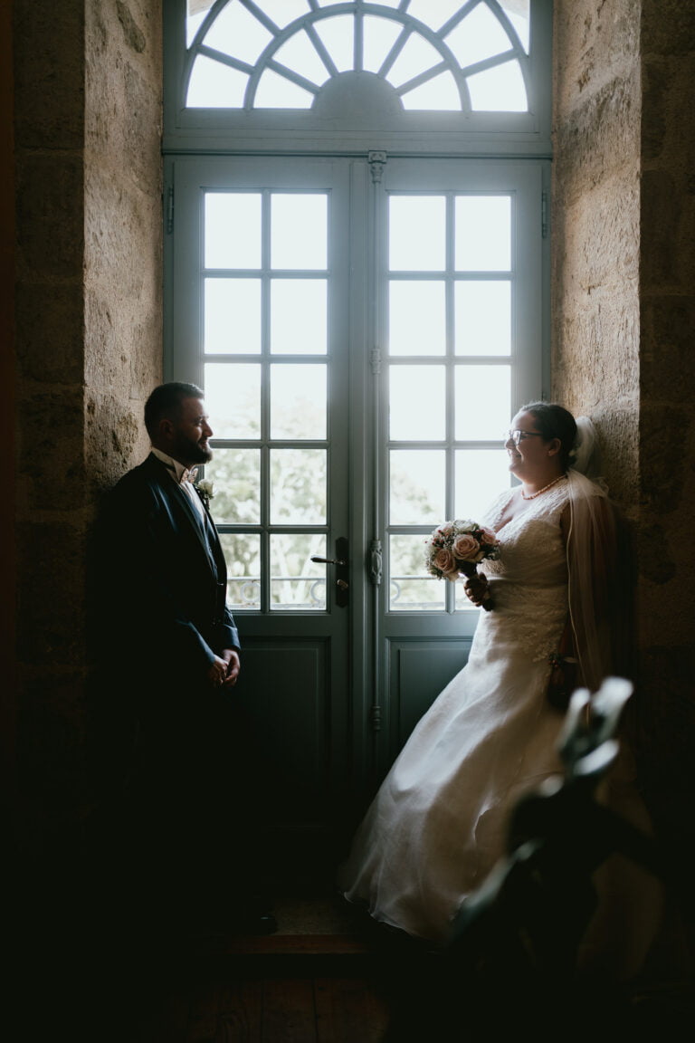 Des mariés debout devant une fenêtre au mariage au château Lacoste.