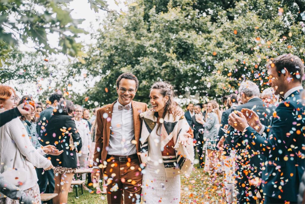Des mariés défilent dans l'allée du mariage domaine Bouhemy en leur lançant des confettis.