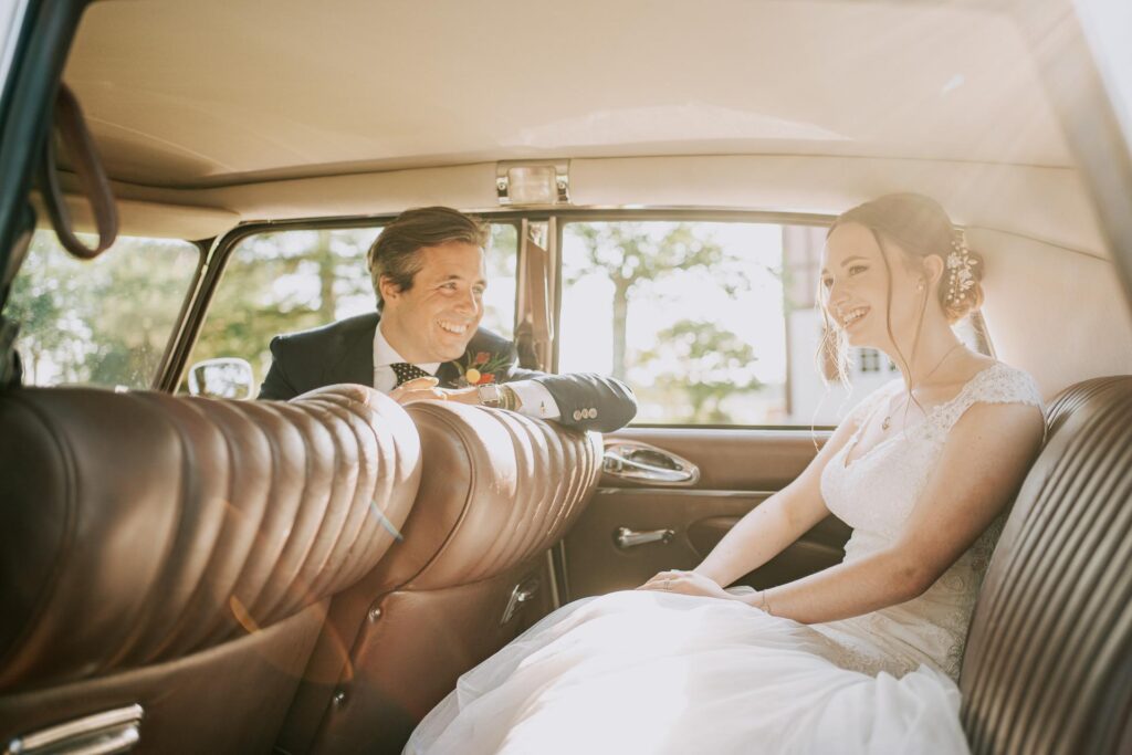 Des mariés assis sur la banquette arrière d'une voiture ancienne, photographiés par un photographe mariage Landes.