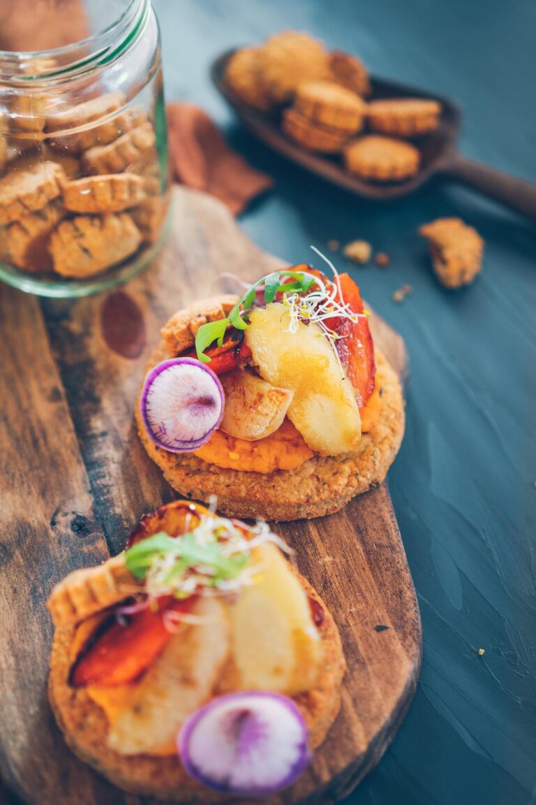 Une planche à découper en bois avec deux sandwichs et un pot de crackers.