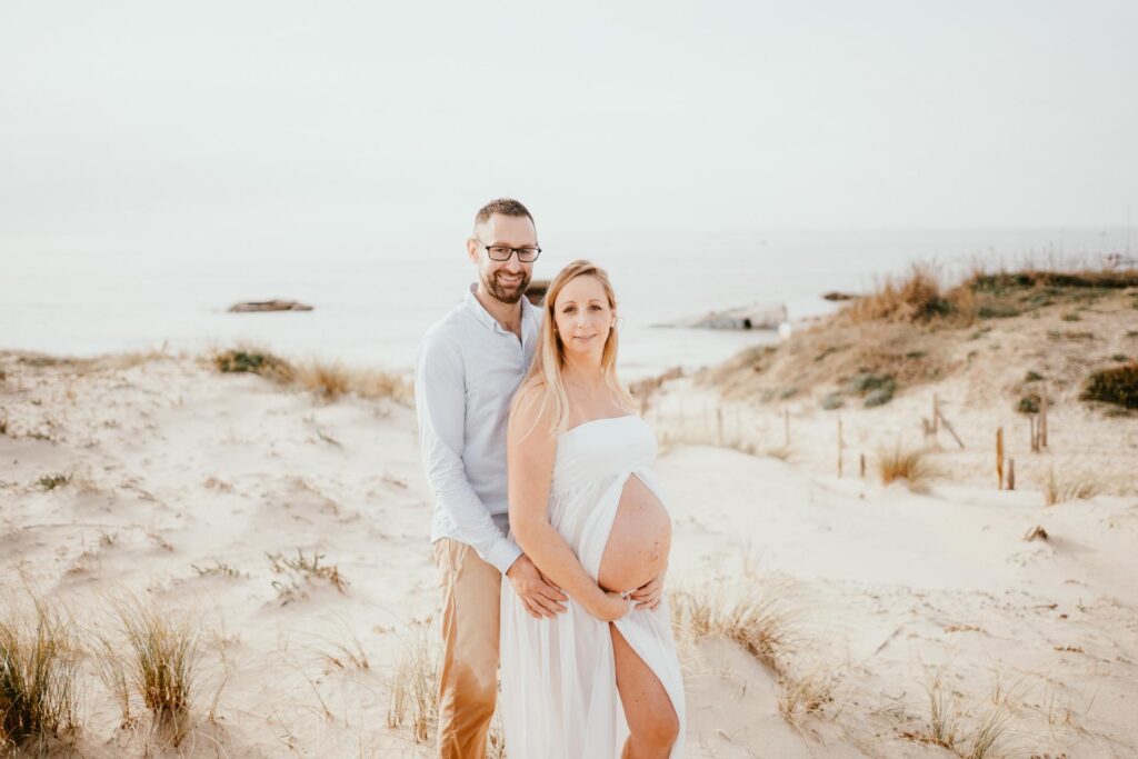 Un couple enceinte debout sur le sable de la plage pour leur séance de photographe grossesse Landes.