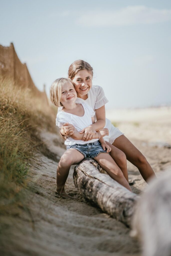 Une mère et sa fille assises sur une bûche sur la plage, font des photos de vacances.