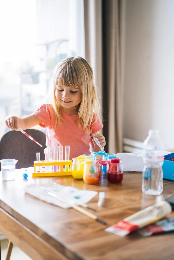 Une petite fille est assise à une table et fait une expérience scientifique, rêvant de faire des photos de vacances.