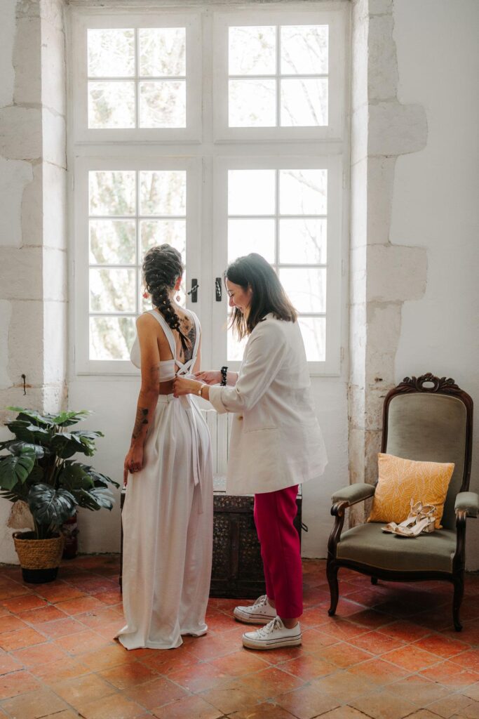 Une femme aide une autre femme à enfiler sa robe de mariée magenta.