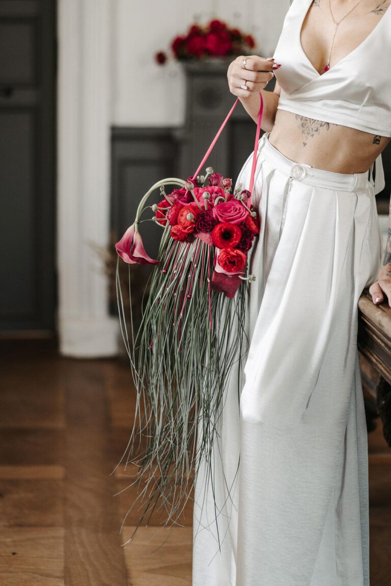 Une femme vêtue d'une robe blanche tenant un bouquet de fleurs magenta.
