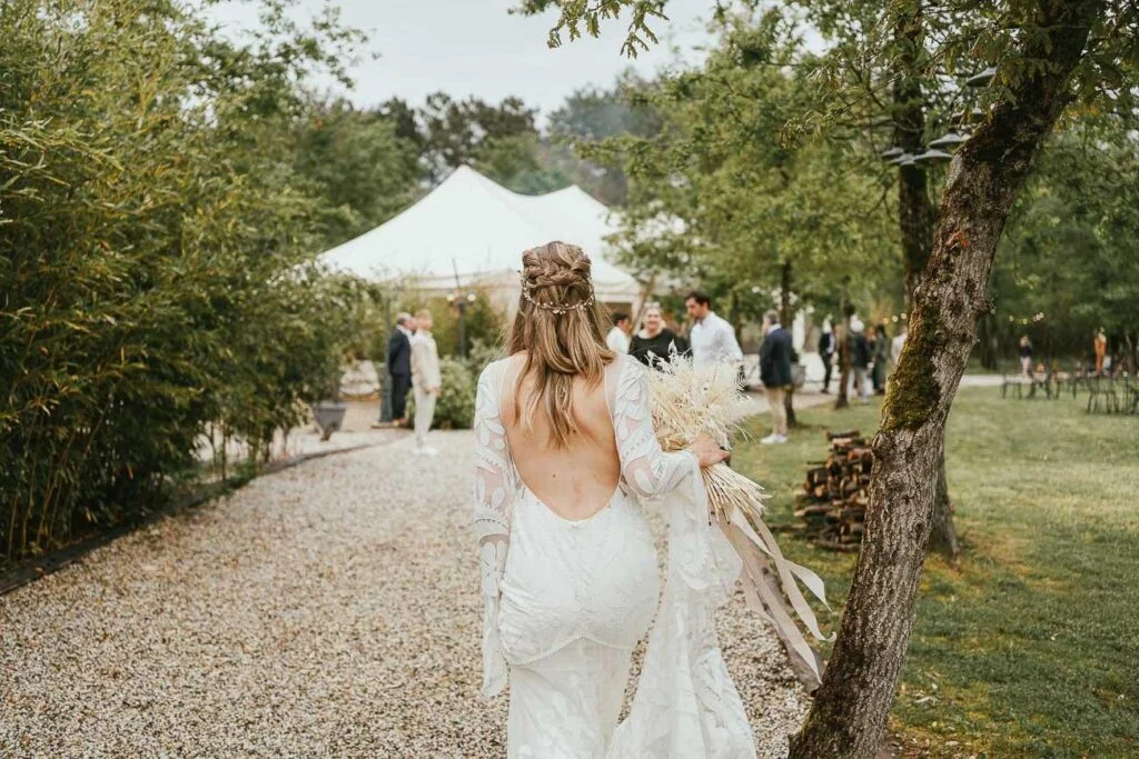 Une mariée marchant dans un chemin du domaine de mariage Petiosse avec une tente en arrière-plan.