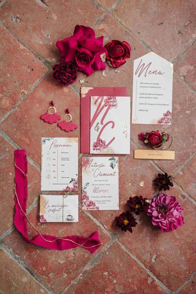 Un ensemble de papeterie de mariage avec des roses et des fleurs magenta sur un sol carrelé, offrant une inspiration pour votre mariage.