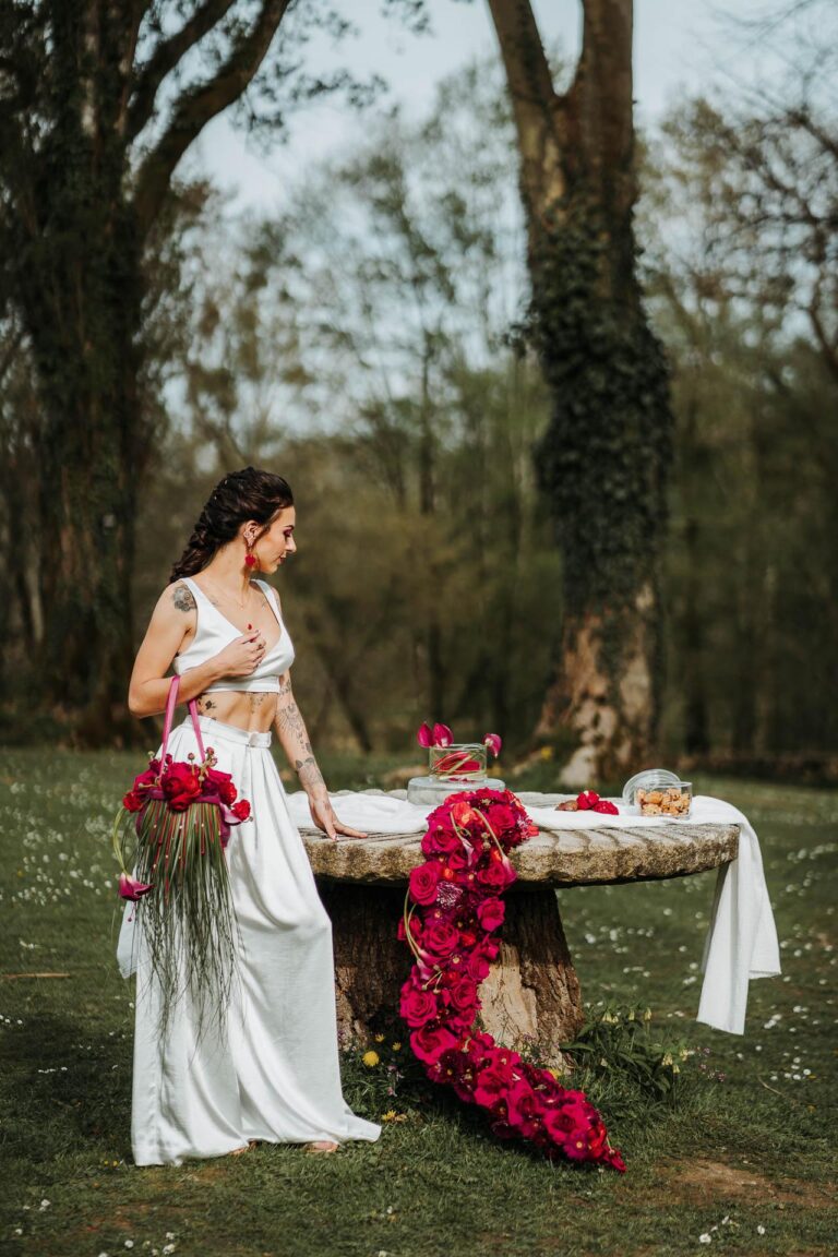 Une femme vêtue d’une robe blanche debout à côté d’une table avec des fleurs magenta.