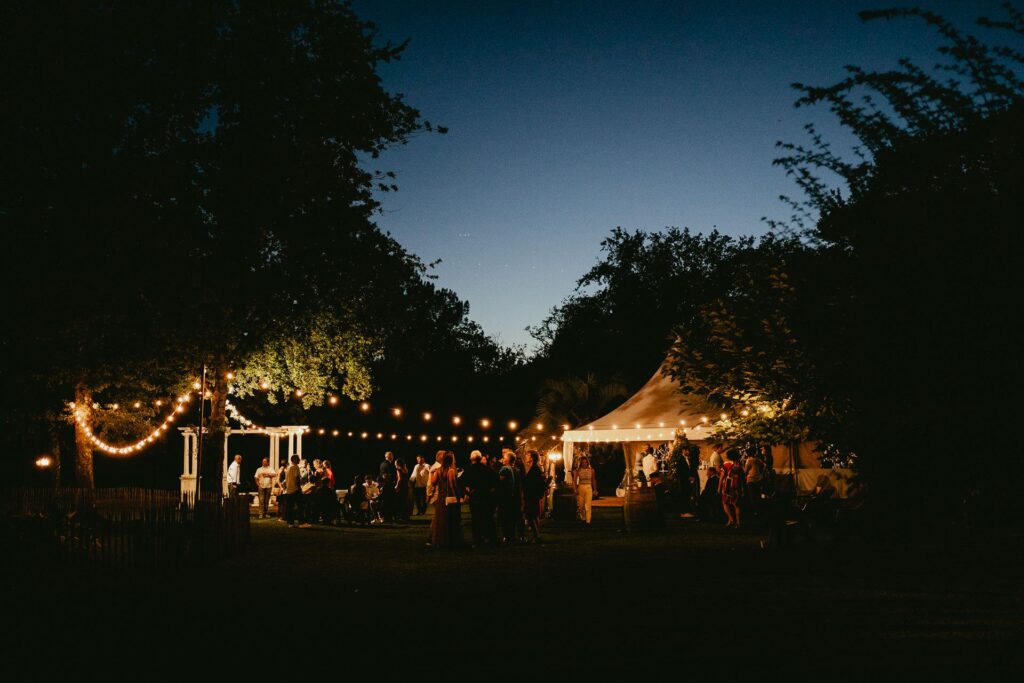 Une réception de mariage biscarrosse en plein air le soir avec des guirlandes lumineuses.