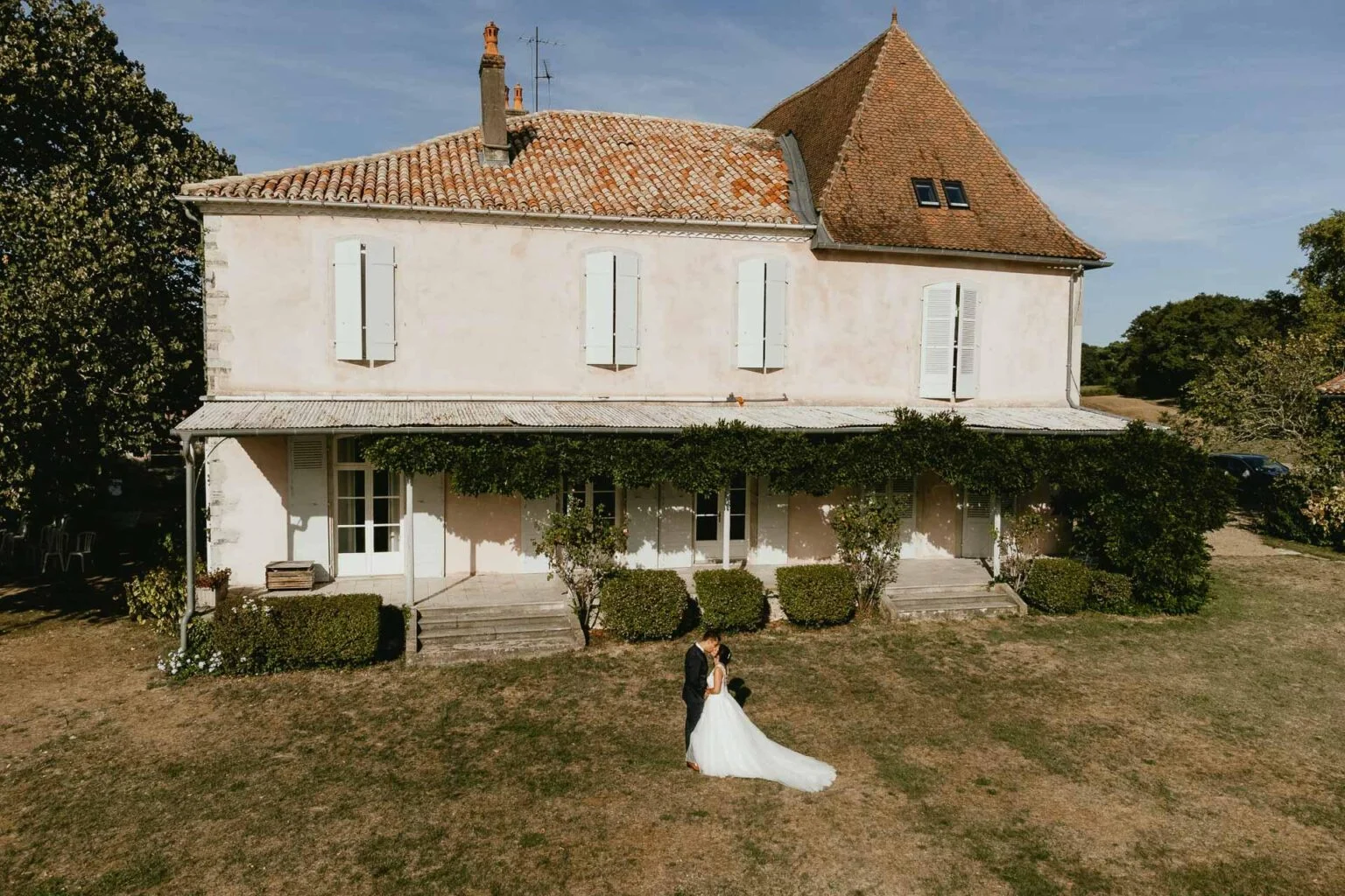 Des mariés debout devant une maison rose lors d’une cérémonie laïque.