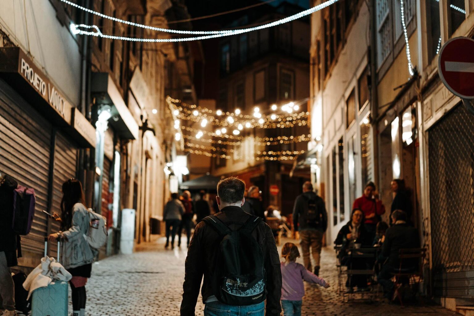 Un homme et un enfant marchant la nuit dans une rue pavée pendant leurs vacances à Porto.
