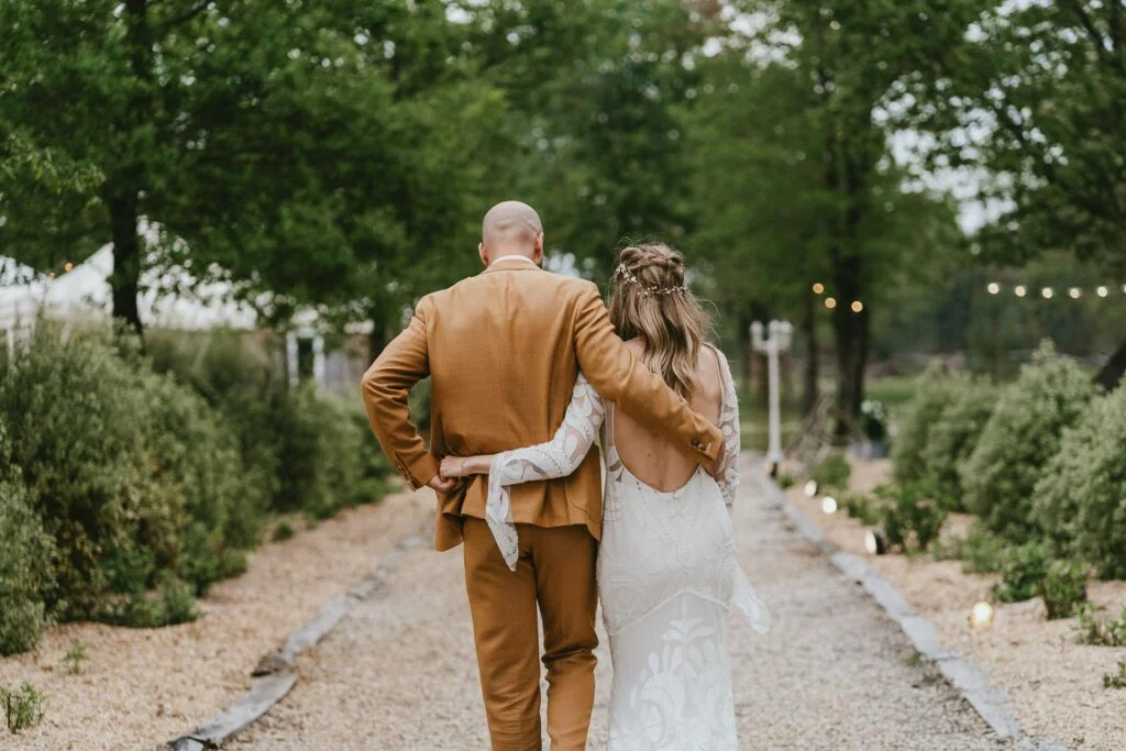 Des mariés marchant dans un chemin en costume beige au mariage domaine Petiosse.