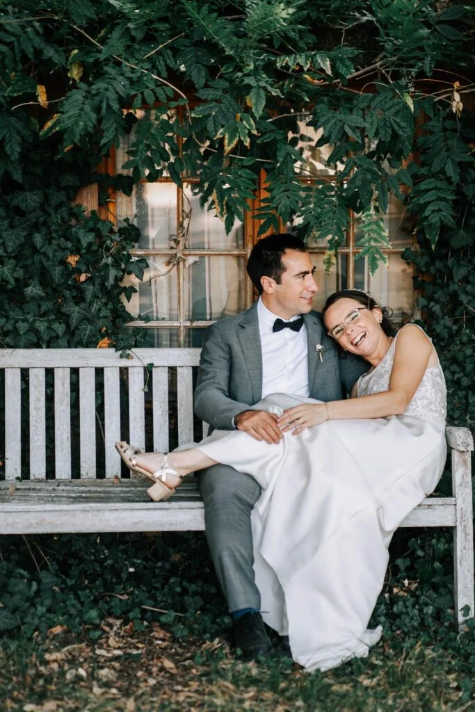 Des mariés sont assis sur un banc en bois dans un jardin, parfait pour capturer des images intemporelles par comment trouver son photographe mariage.