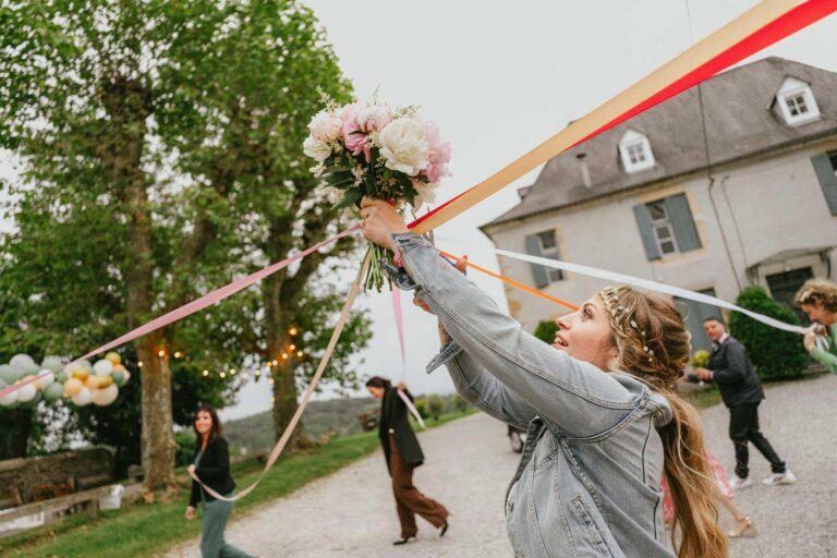 Une femme tient un bouquet devant une maison, habillée pour son mariage hippie.