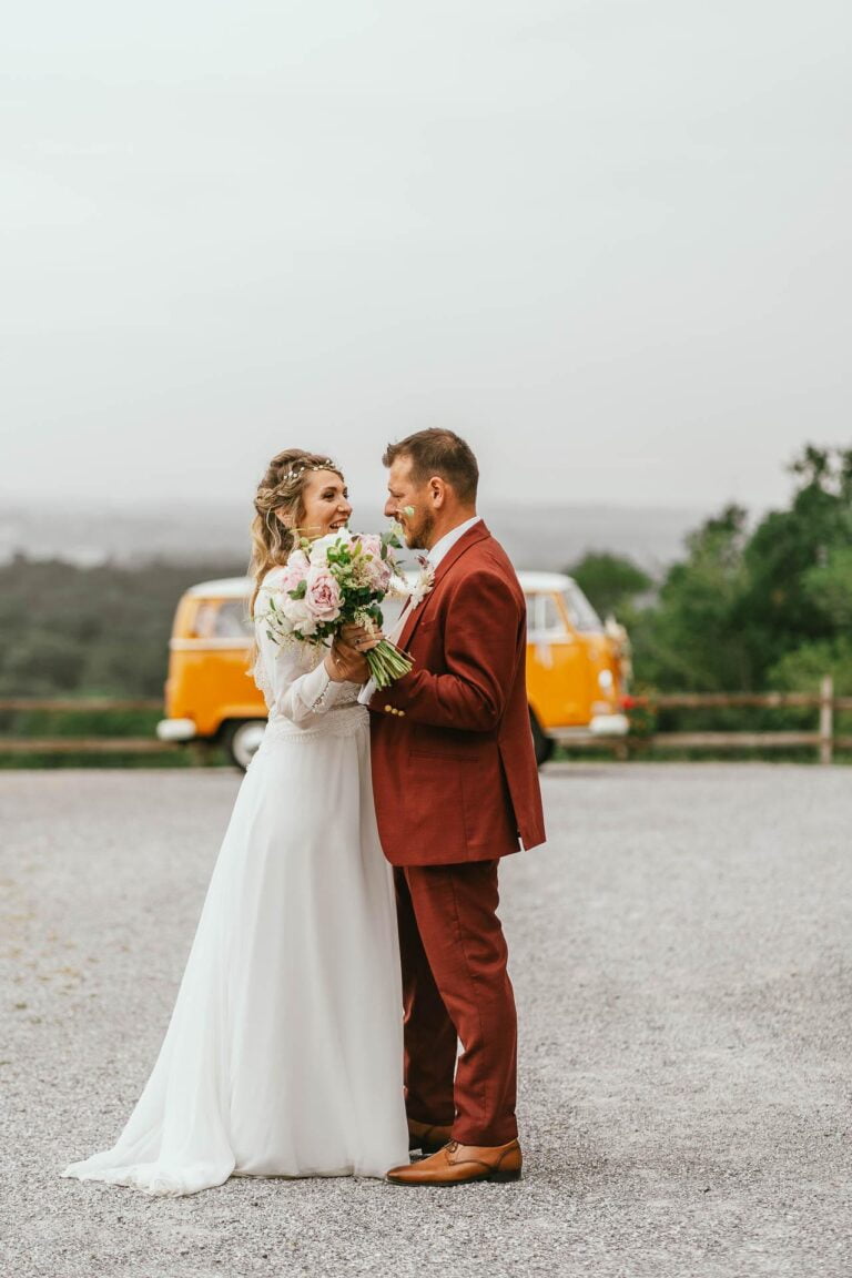 Des mariés debout devant un bus VW lors de leur mariage hippie.