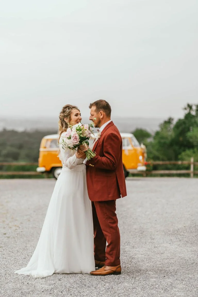 Des mariés debout devant un bus VW lors de leur mariage hippie.