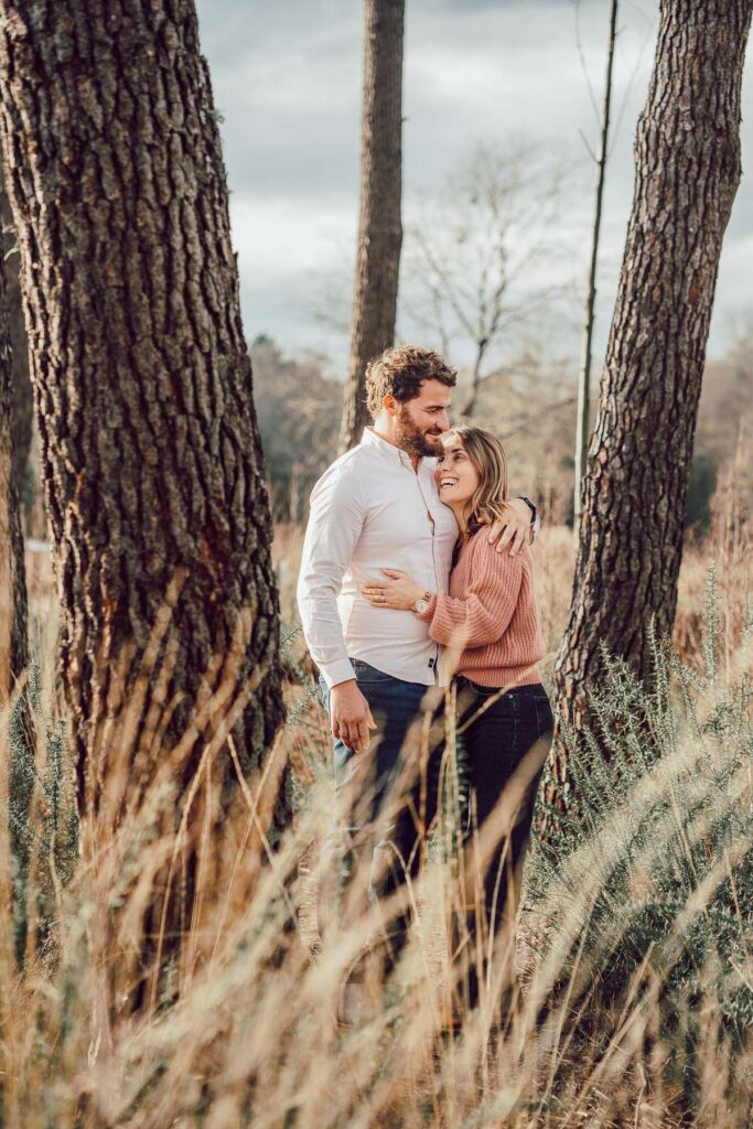 Un couple fiancé s'embrassant dans un champ de grands arbres.