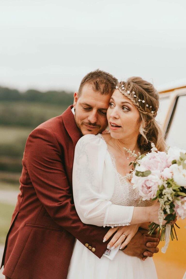 Des mariés s'embrassant devant un bus VW lors de leur mariage hippie.