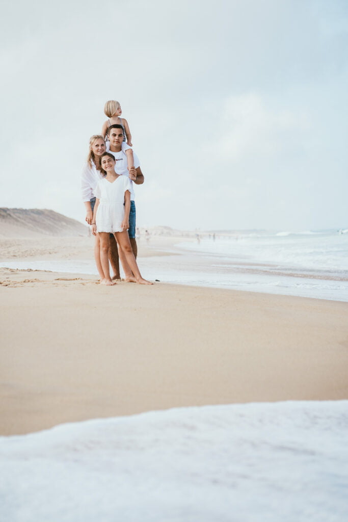 Une famille se tient sur la plage face à l’océan.