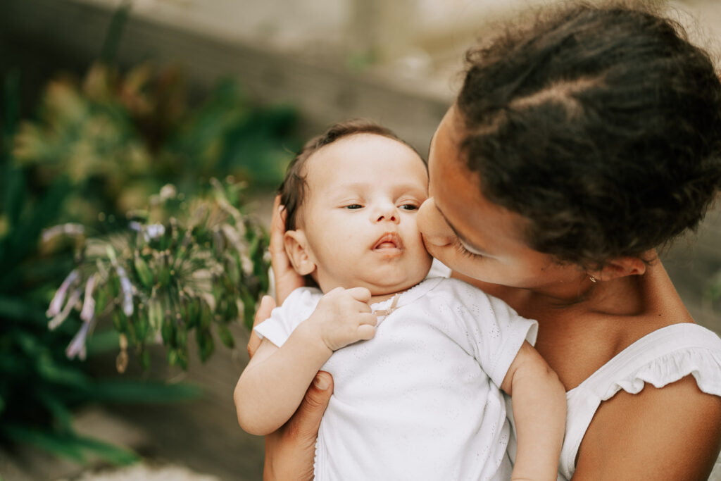 Une femme embrasse son bébé devant des plantes.