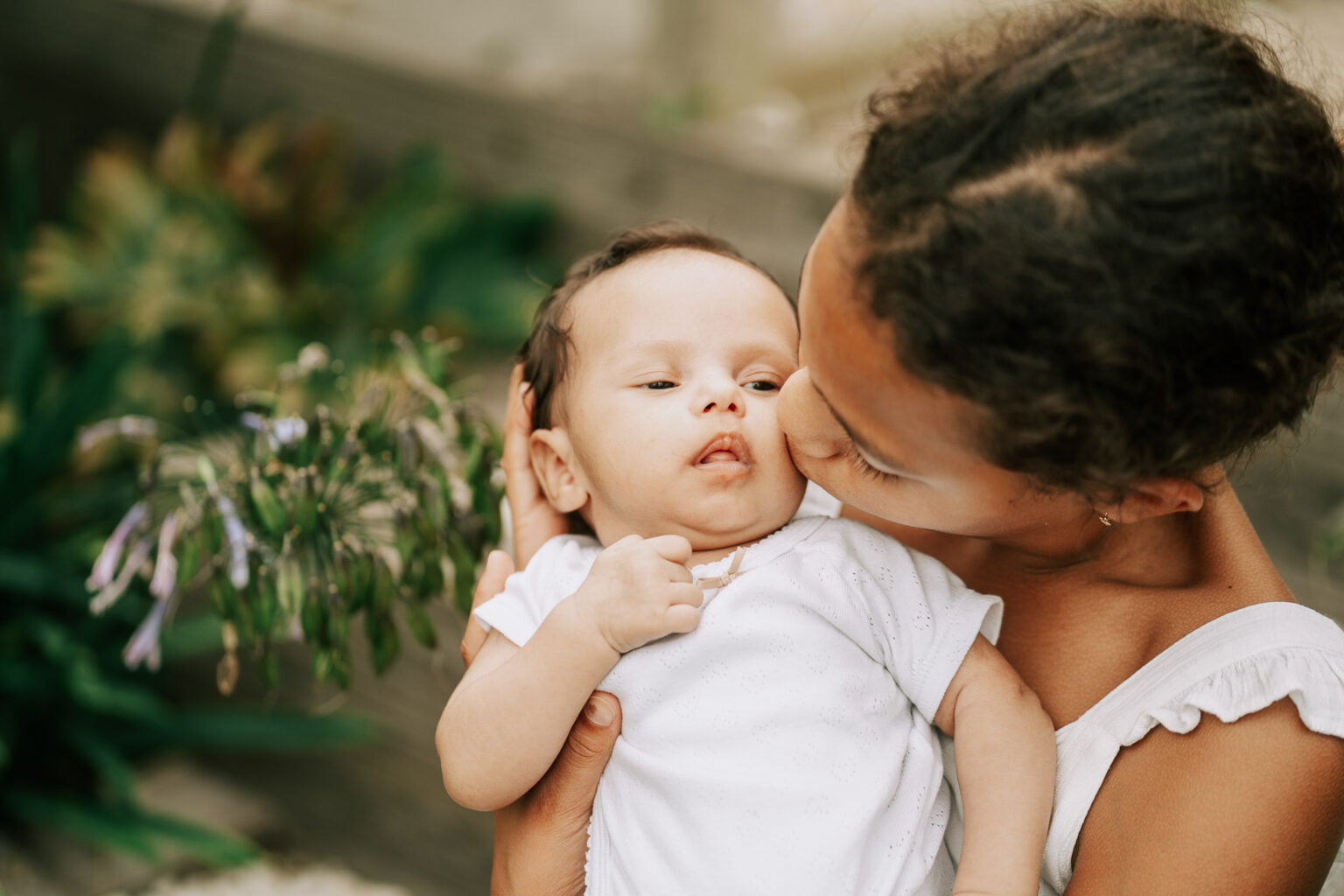 Une femme embrasse son bébé devant des plantes.
