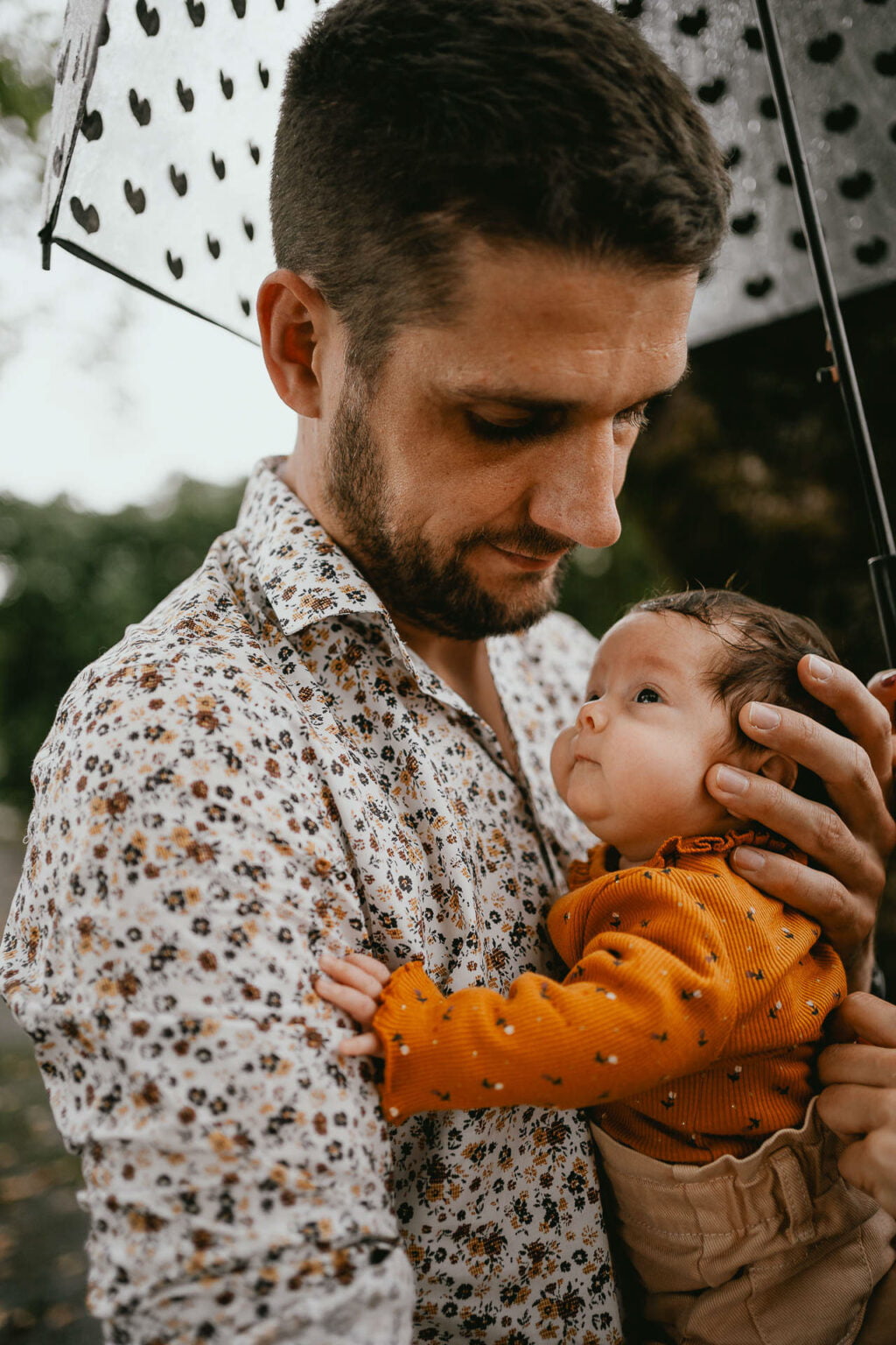 Un homme tenant un bébé sous un parapluie.