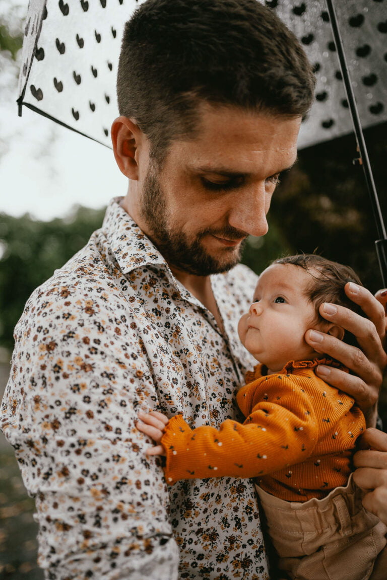 Un homme tenant un bébé sous un parapluie.