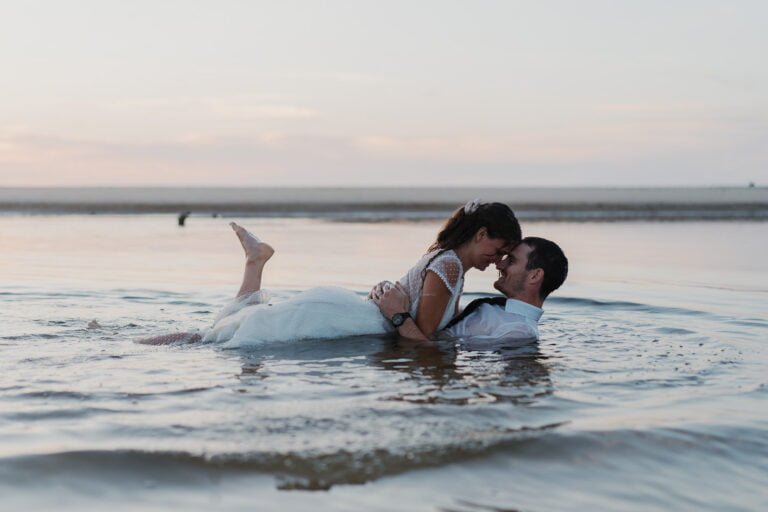 Une mariée et un marié s'embrassant dans l'eau au coucher du soleil.