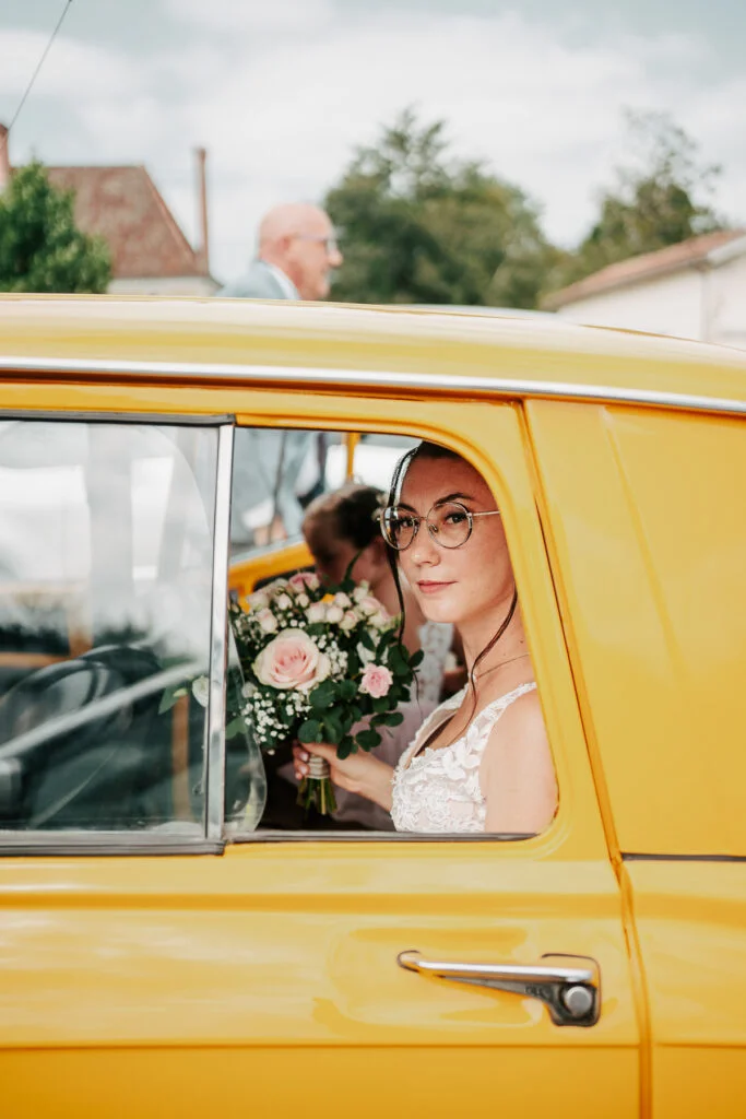 Une mariée est assise sur la banquette arrière d’une voiture jaune.