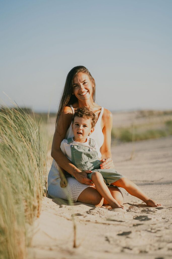 Une femme et son fils assis sur le sable à la plage pendant une séance photo.