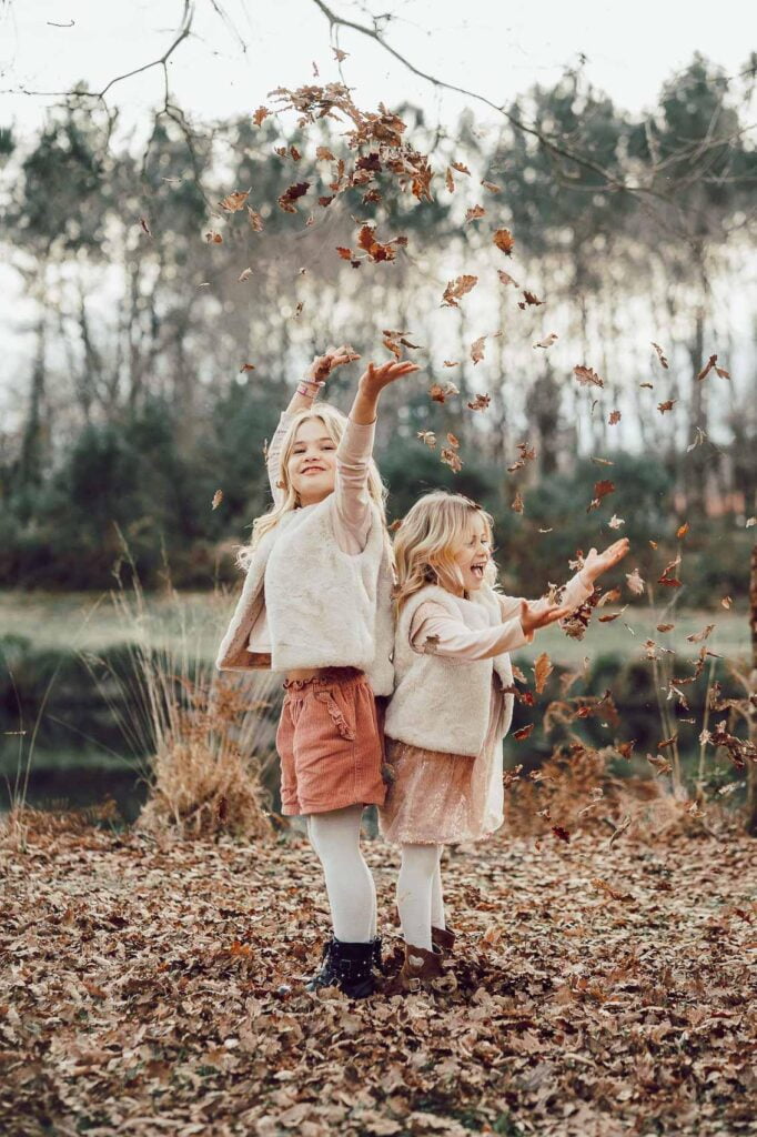 Deux petites filles profitant d'une séance photo dans les Landes, jouant avec les feuilles dans un parc.