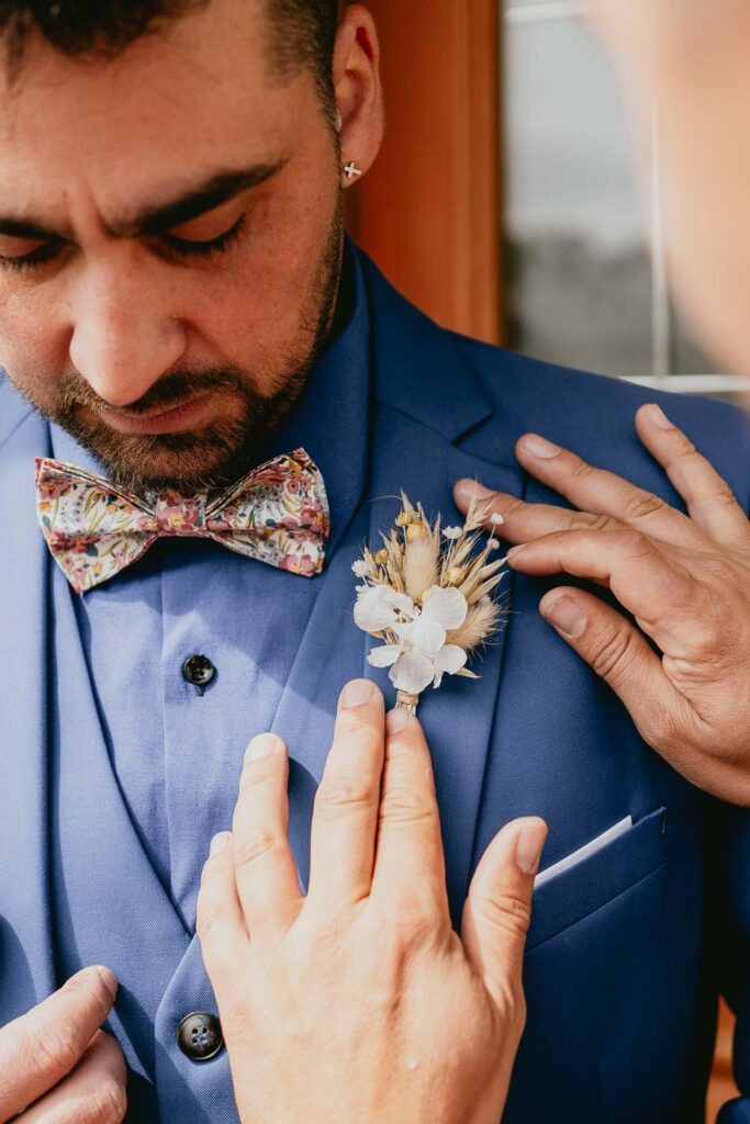 Un homme en costume bleu ajuste sa boutonnière pour un mariage hippie.