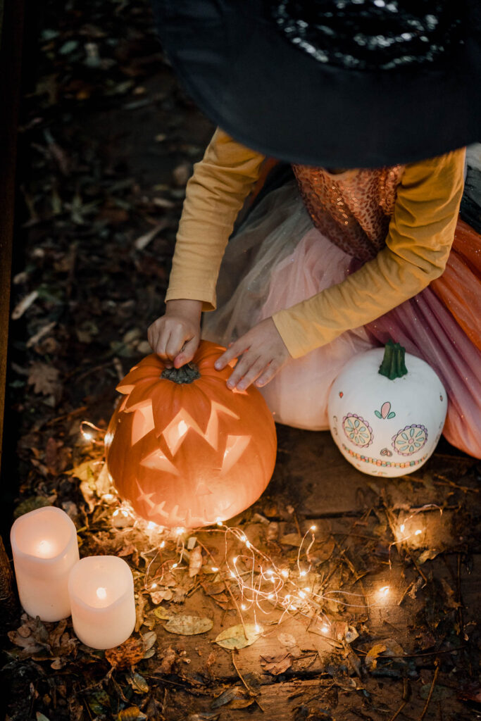 Une fille avec un chapeau de sorcière décorant une citrouille pour une séance photo d'Halloween.