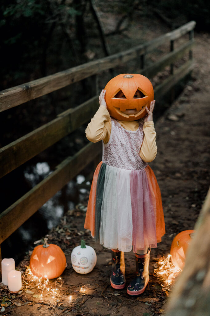 Une petite fille vêtue d'une robe avec une citrouille sur la tête pose pour une séance photo d'Halloween.