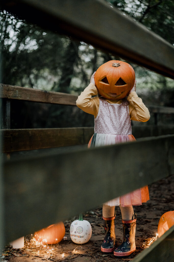 une petite fille a posé une citrouille d'halloween sur la tête.