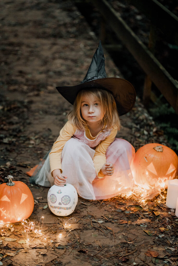 Une petite fille déguisée en sorcière est assise autour de citrouilles d'Halloween