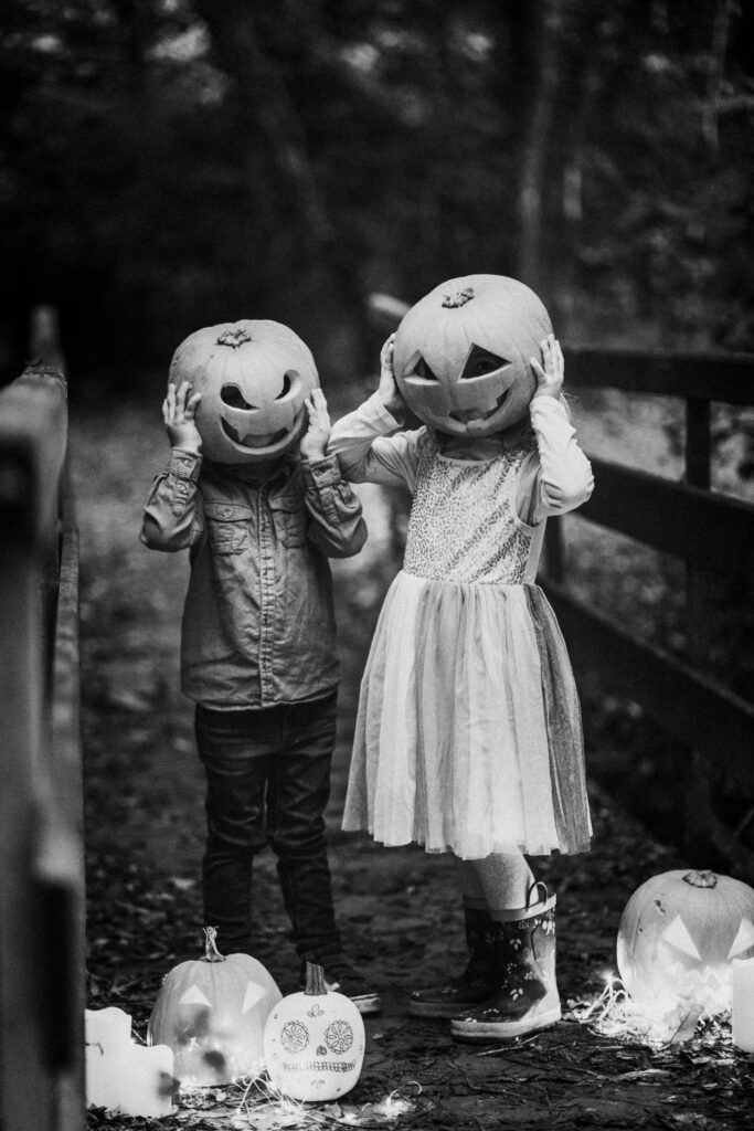 Photo en noire et blanc de deux enfants qui ont une citrouille d'Halloween sur la tête et qui nous regardent.