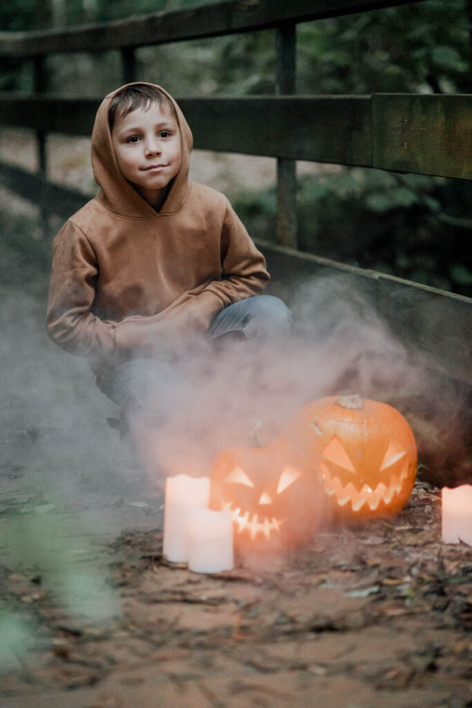 Un garçon en sweat à capuche est assis sur un pont à côté d'une lanterne citrouille pour une séance photo d'Halloween.