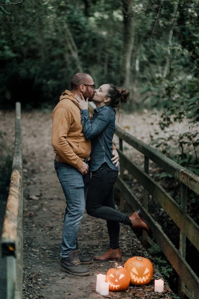 Un couple s'embrassant sur un pont avec des citrouilles en arrière-plan lors d'une séance photo d'Halloween.