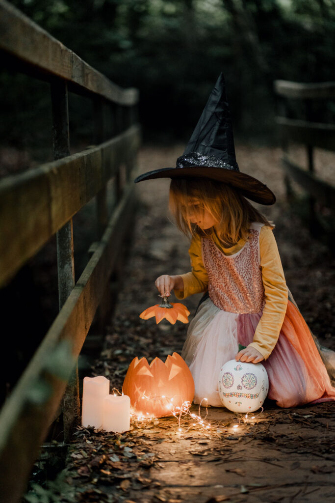 Une petite fille déguisée en sorcière regarde à l'intérieur d'une citrouille.