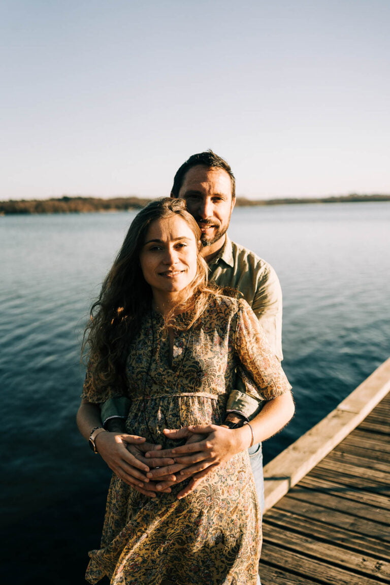 Un couple enceinte debout sur un quai au bord d’un lac.