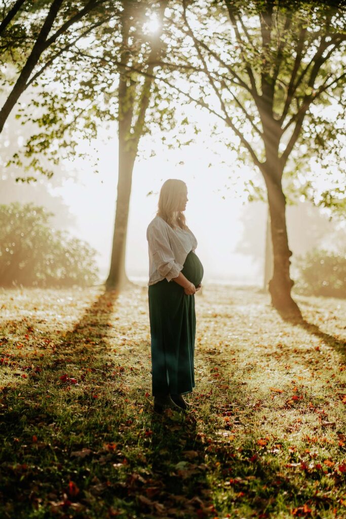 Une femme enceinte debout dans un parc avec des arbres en arrière-plan.