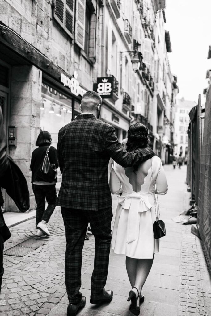 Une photo en noir et blanc d'un couple marchant dans une rue pour être témoin d'un mariage.