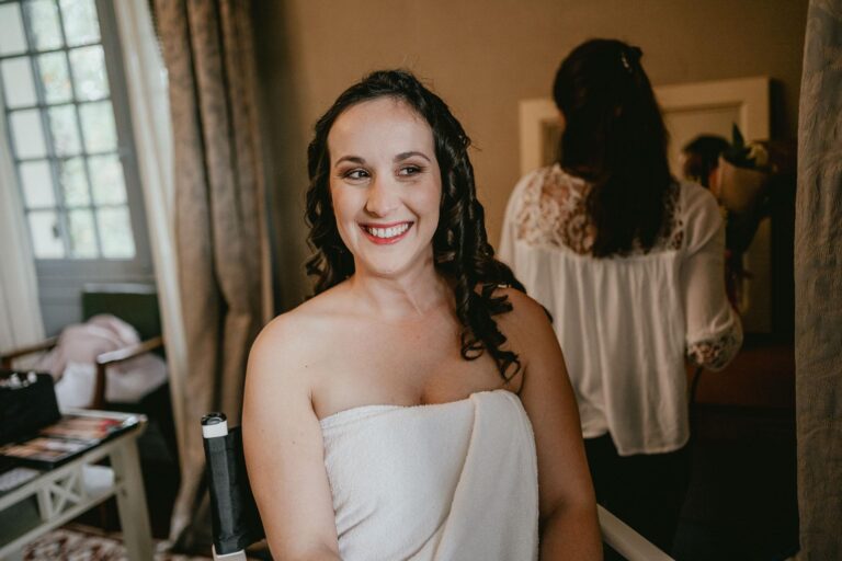 Une mariée en robe blanche souriant devant un miroir, prête à être témoin de mariage.