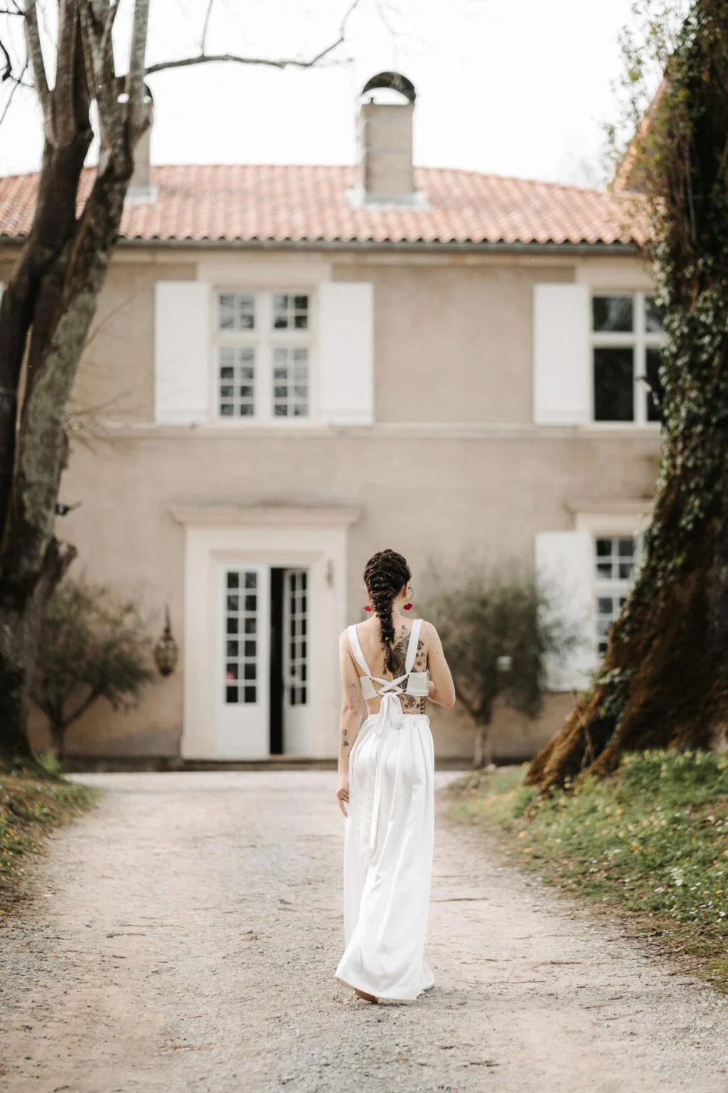 Une mariée, habillée par une couturière, marchant dans un chemin devant une maison pour son mariage dans les Landes.