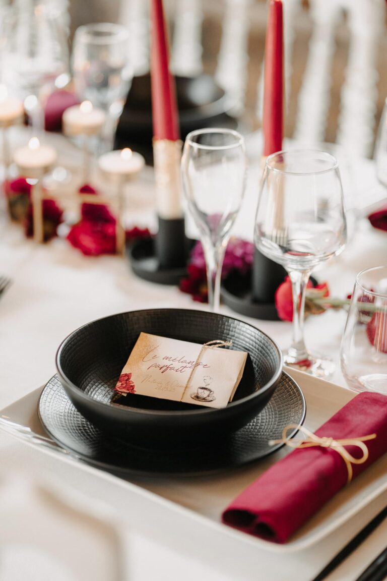 Une table dressée avec des assiettes noires et rouges, des bougies et une papeterie mariage landaise.