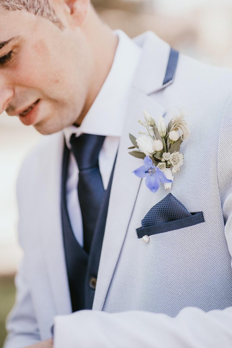 Un homme en costume blanc avec une boutonnière fleuriste bleue.