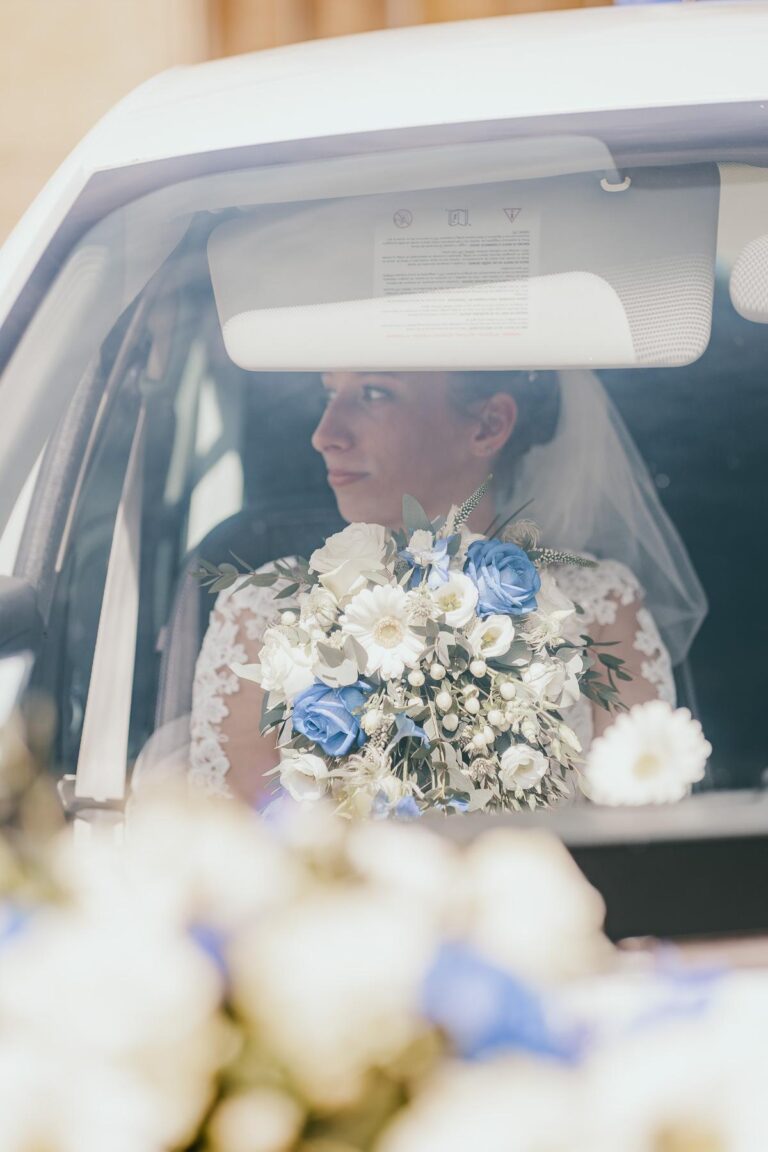Une mariée est assise sur la banquette arrière d'une voiture, tenant un bouquet du fleuriste mariage landais.