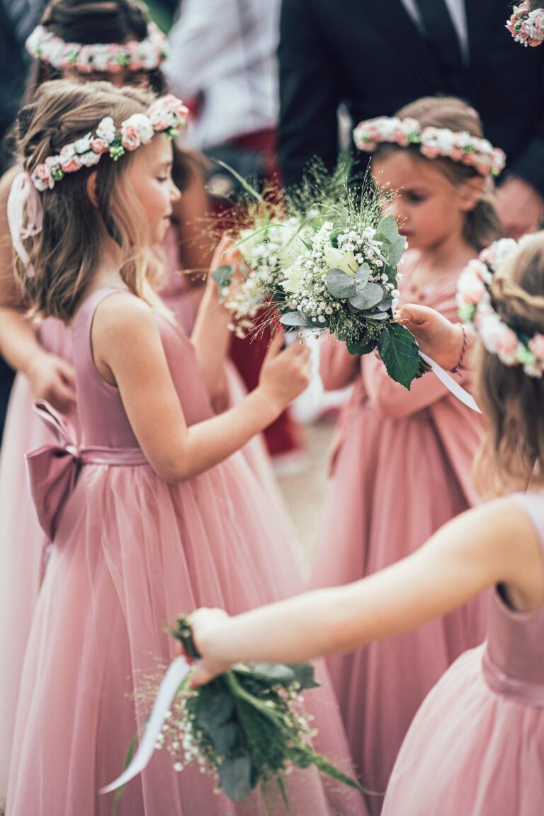 Un groupe de petites filles en robes roses tenant des couronnes de fleurs fleuristes.